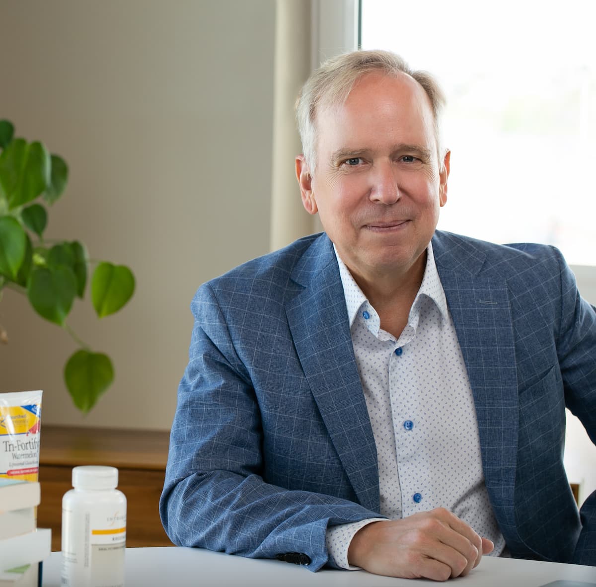 Dr. Marty Ross, MD, author of "Our Story," smiles seated at a desk with health products.